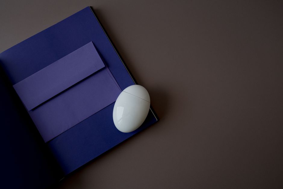 A minimalist composition featuring a blue folder, envelope, and an egg-shaped device on a gray background.